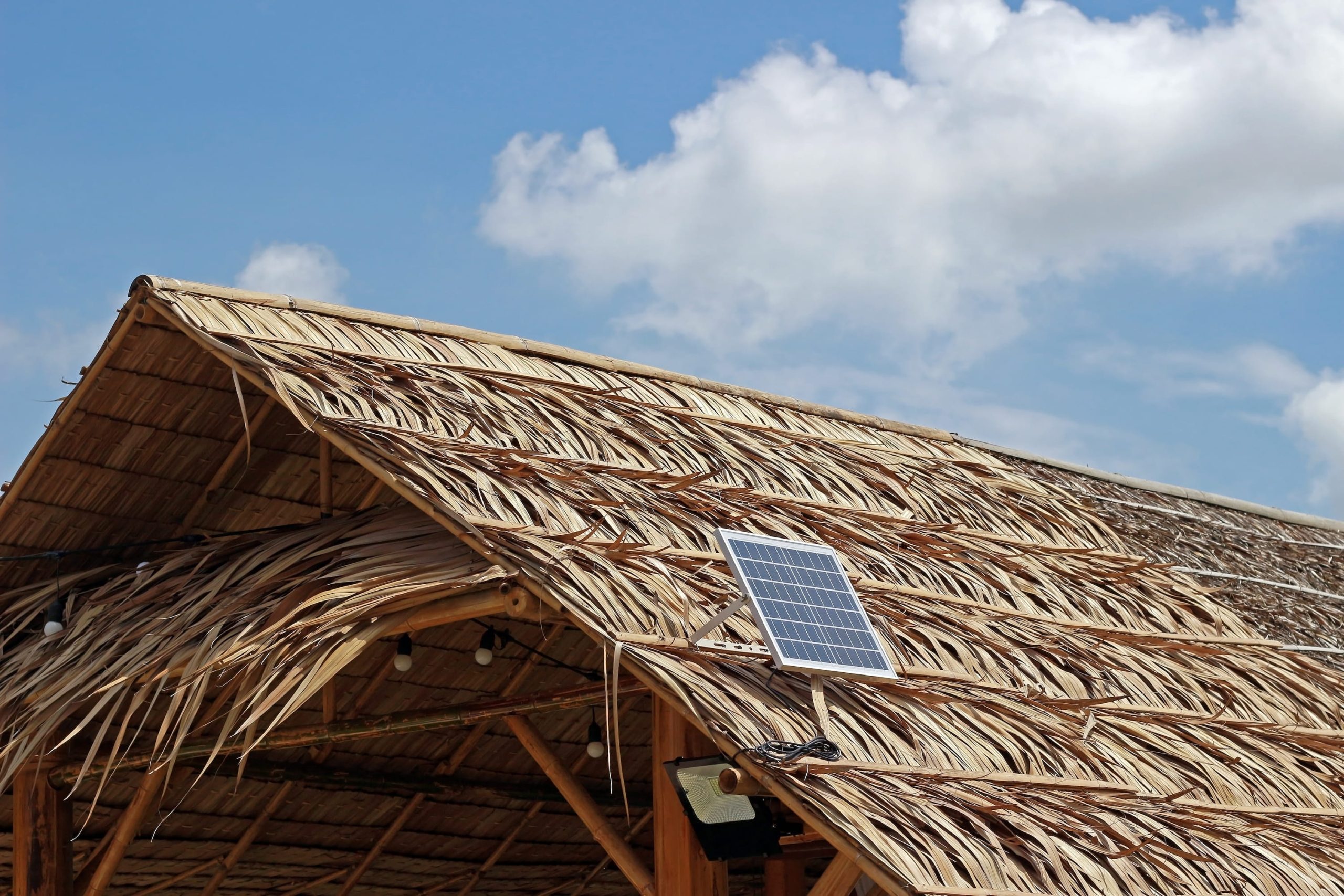 Solar panel with an IOT system on a thatched roof against a partly cloudy sky.