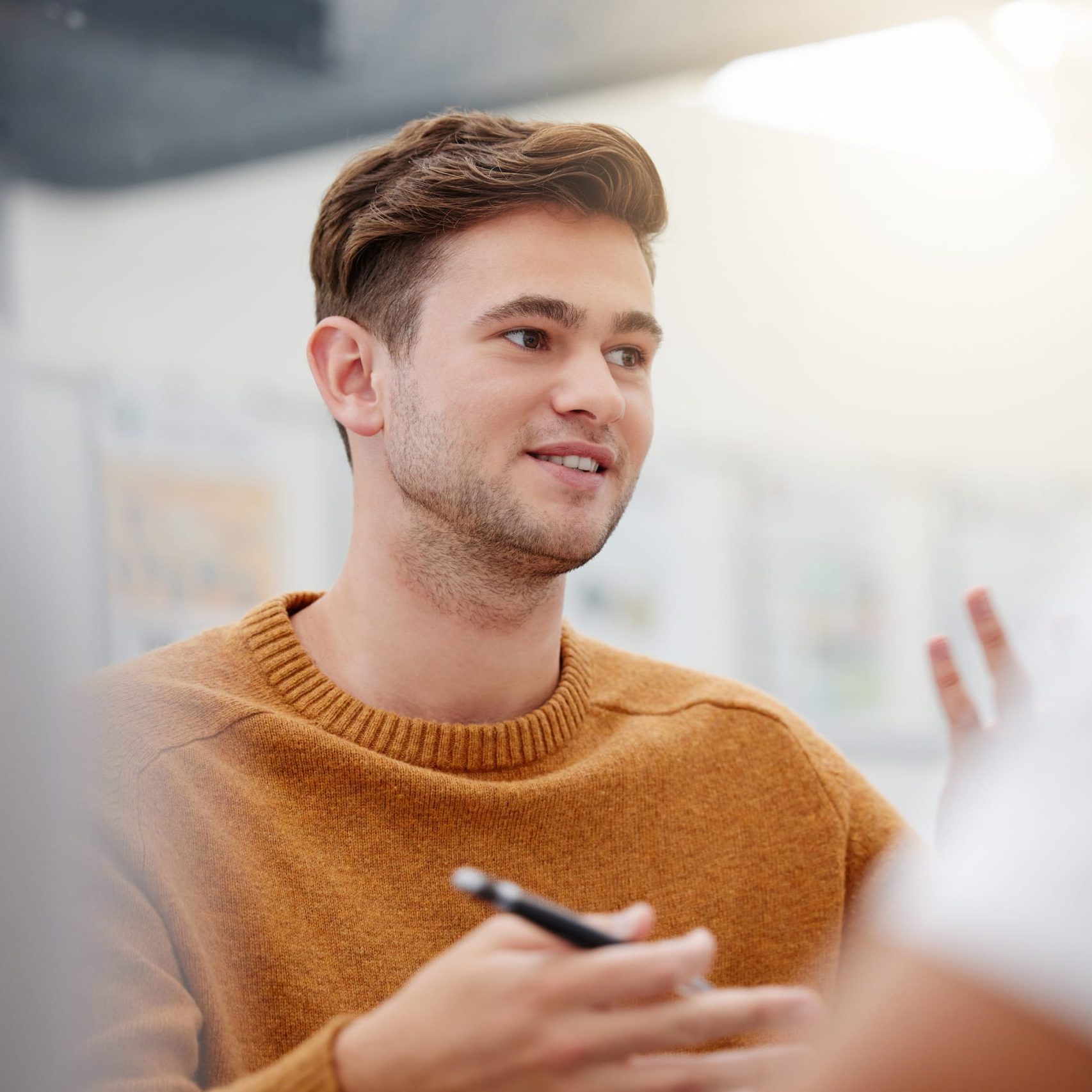 Man in a mustard colour sweater, engaged in conversation with a colleague at the IoT company.