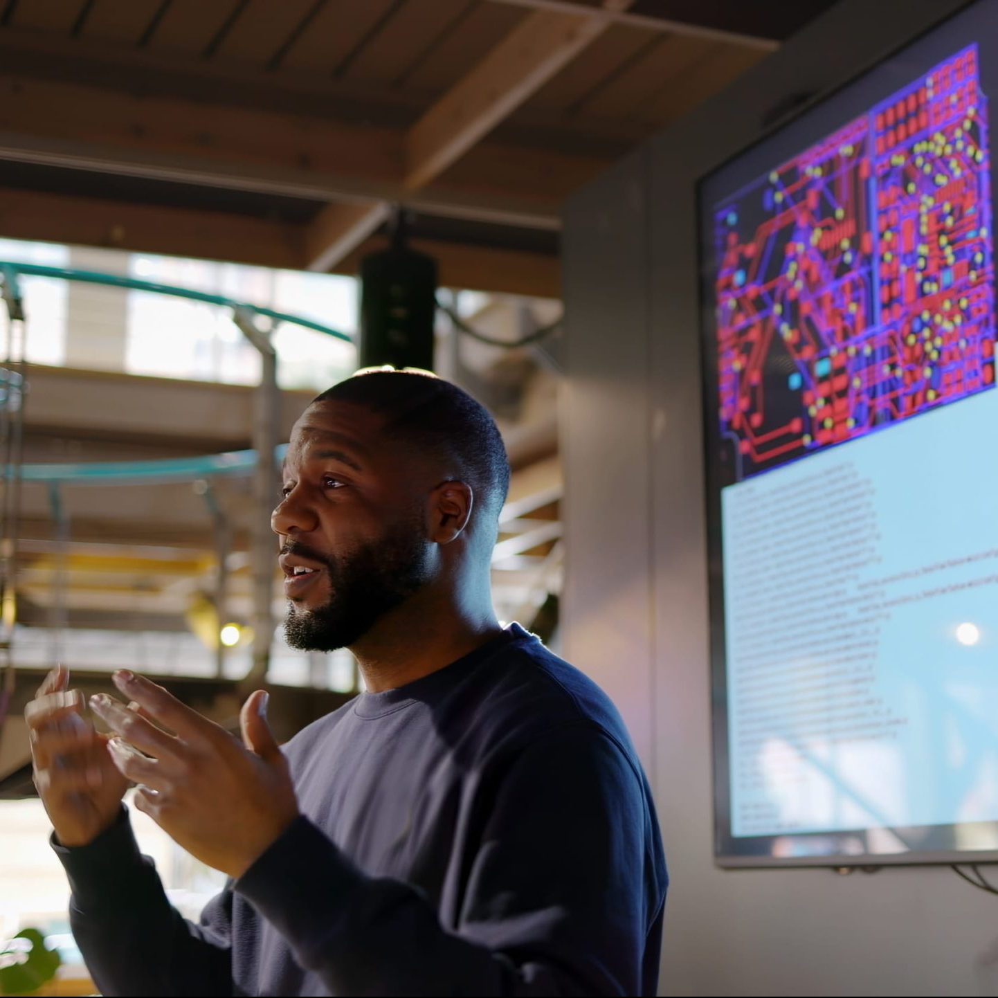 Man presenting an IOT technical topic with code displayed on a screen in the background.